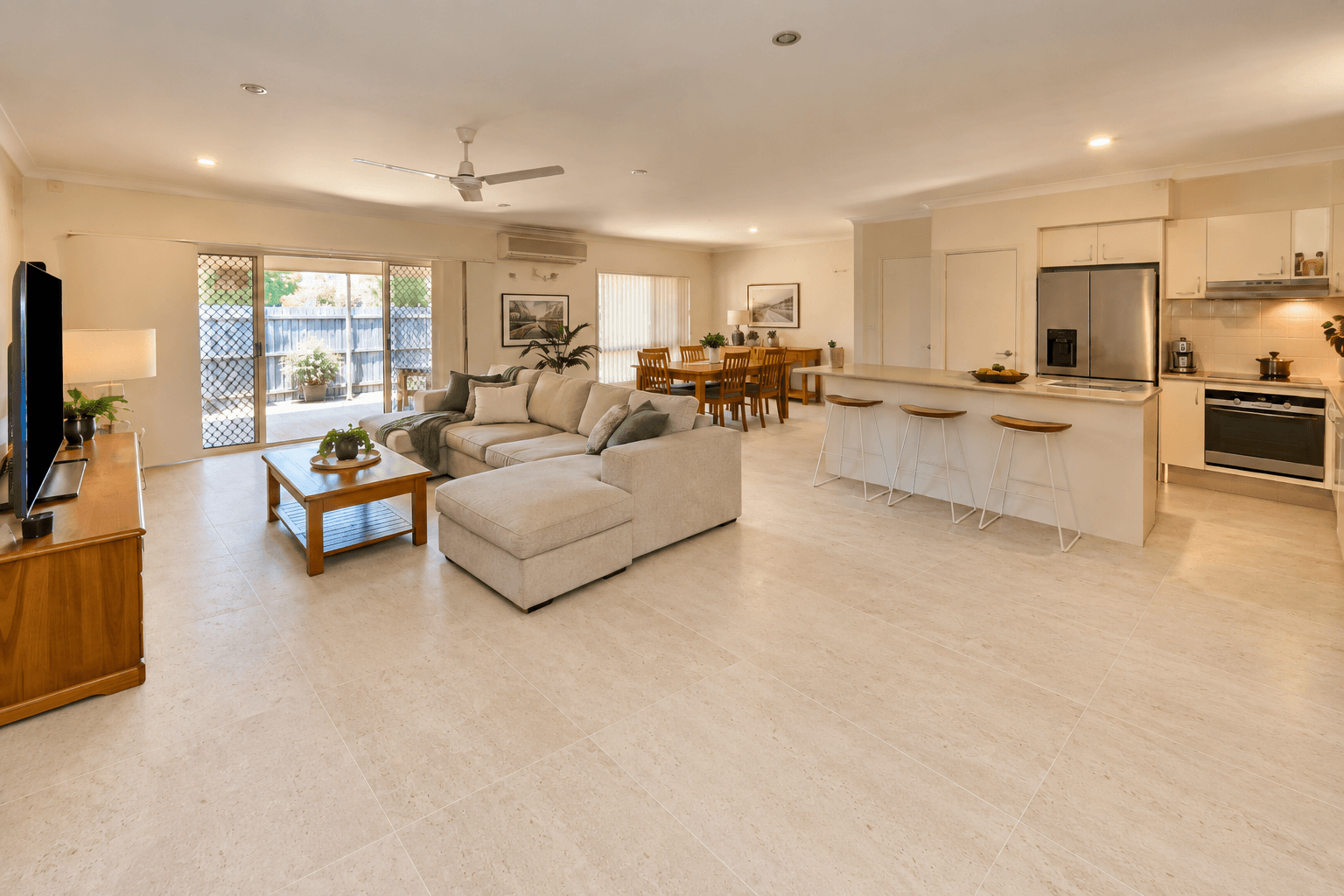 An open-plan living floor, retiled. Carpet out. Large-format ivory stone-look floor in, running through to the kitchen.