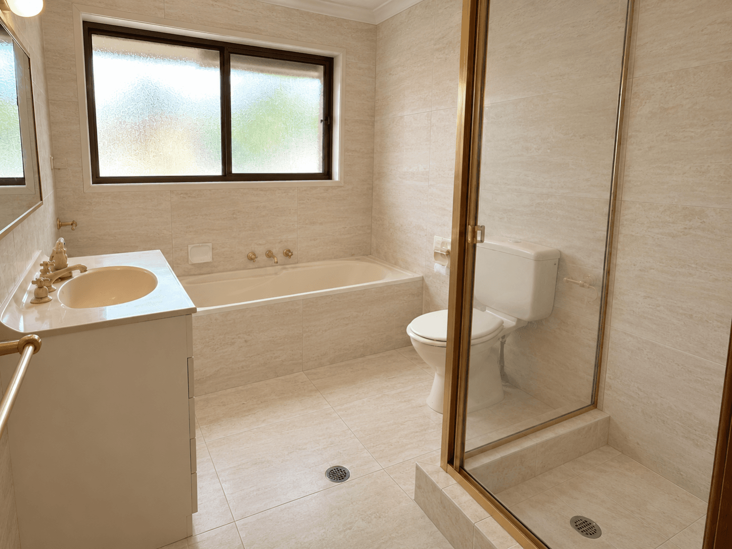 A main bathroom, retiled. Pink tile and floral border out. Ivory travertine-look walls and floor in. Fittings kept.